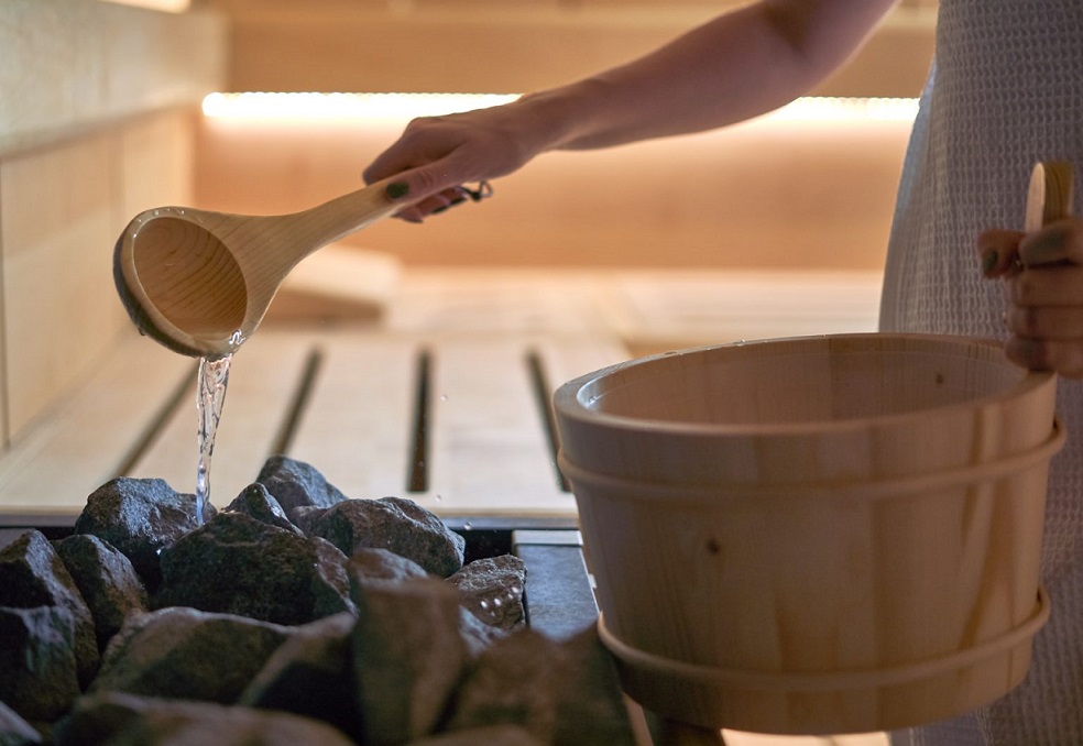 Woman pouring water into hot stone in sauna room.